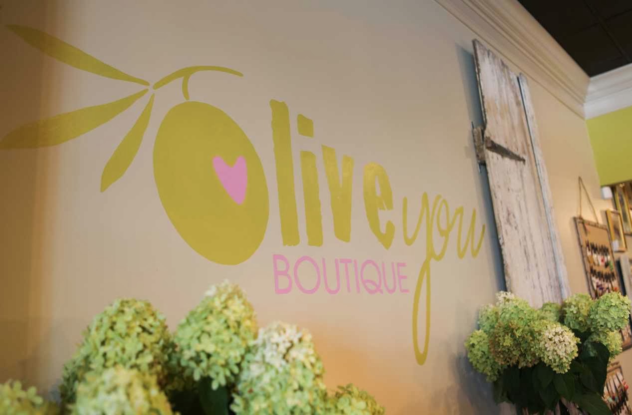 Decorative wall with 'Olive You Boutique' sign and floral arrangements.